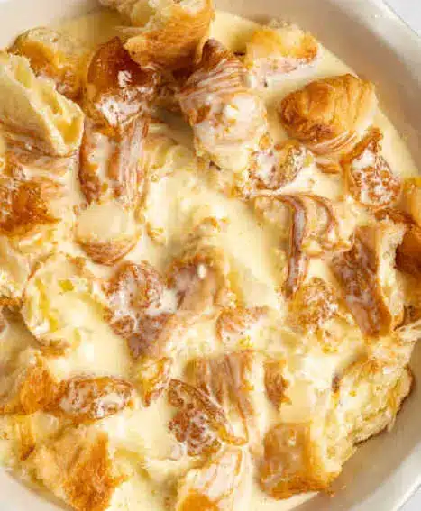 A slice of orange croissant breakfast bake served on a plate with a drizzle of syrup and a sprig of mint.