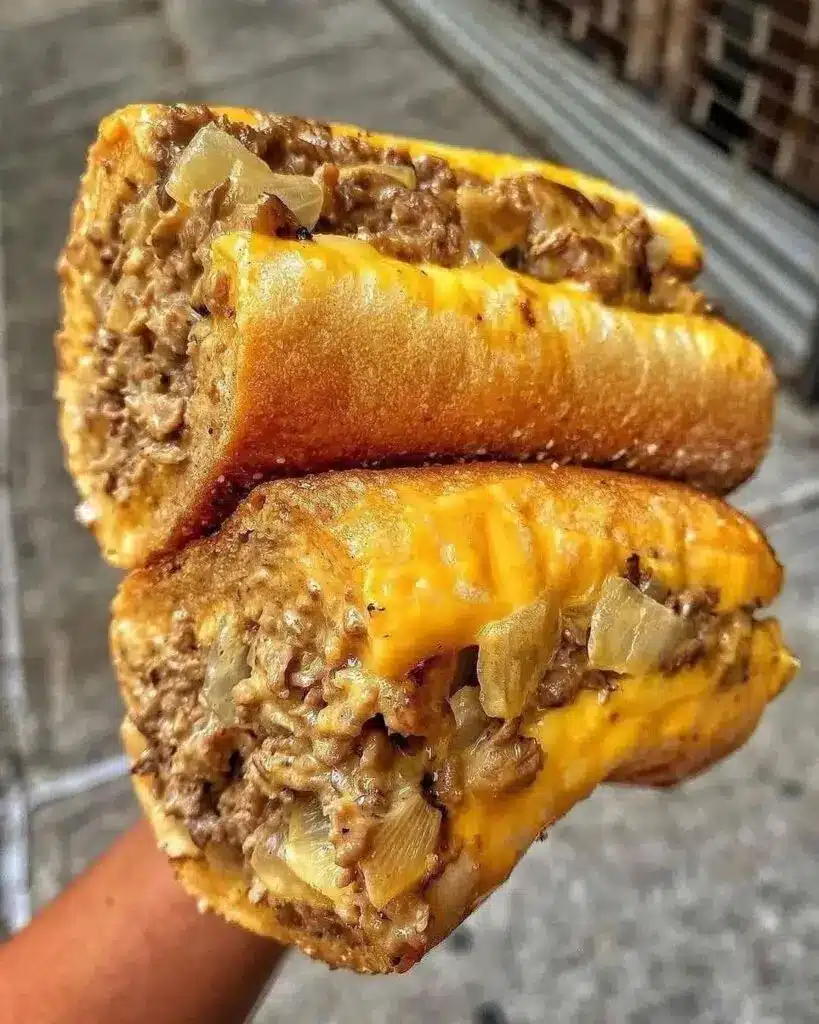 Two Philly cheesesteak sloppy joe sandwiches on toasted buns with a side of potato chips
