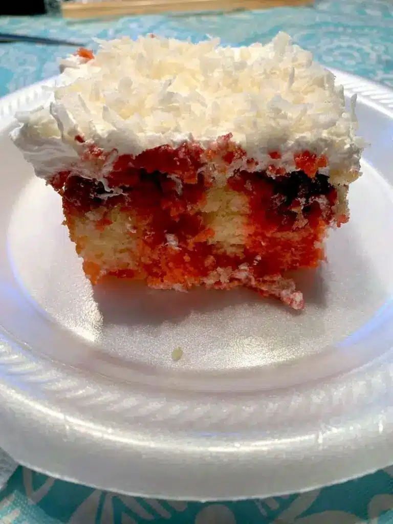A slice of raspberry zinger poke cake showing the internal red streaks and coconut topping.