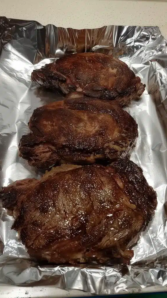 Sliced ribeye steak drizzled with a rich red wine reduction on a dark wooden board