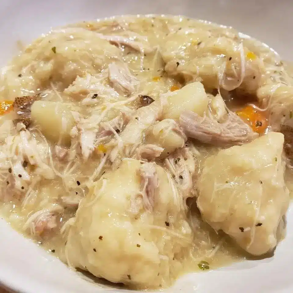 A bowl of slow cooker chicken and dumplings garnished with fresh parsley and black pepper.