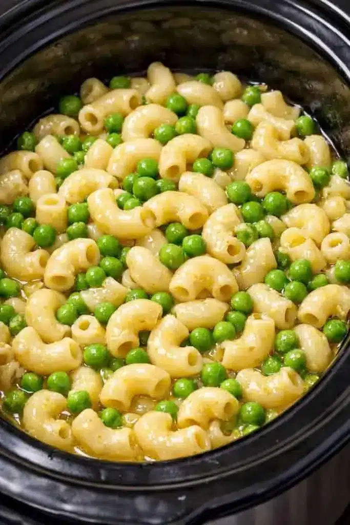 A bowl of creamy macaroni and cheese with sweet peas garnished with black pepper