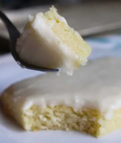 A finished white Texas sheet cake sliced into squares, showing the moist crumb and smooth almond frosting.